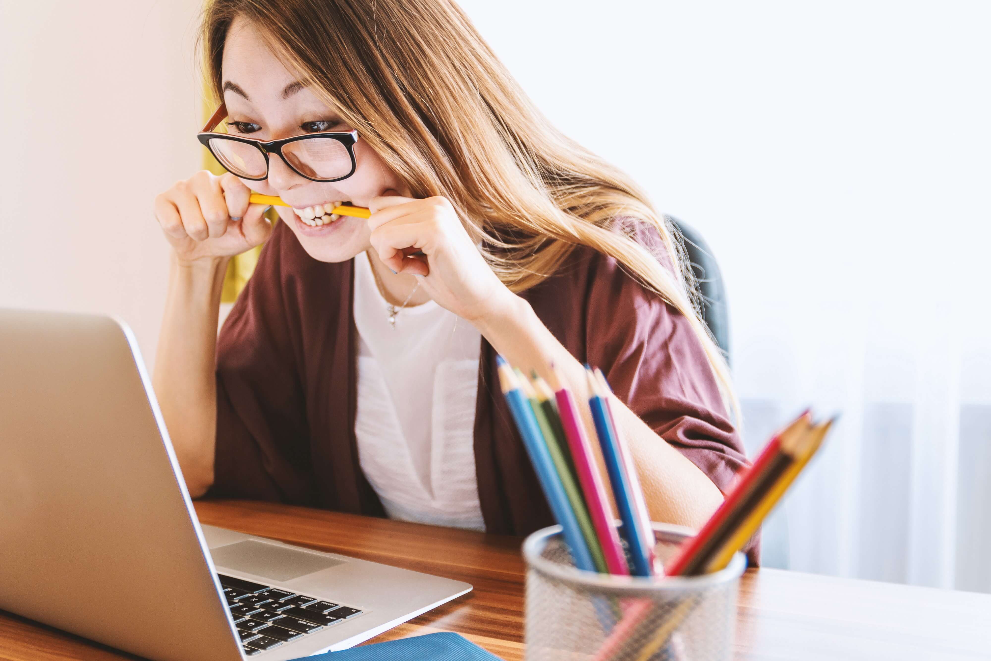 Woman biting a pen in front of a laptop